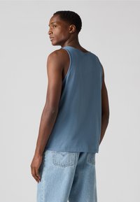 Débardeur bleu clair à coupe décontractée, fabriqué en coton doux. Présente de larges emmanchures et un ourlet droit, associé à un jean en denim délavé.