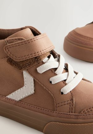 Pruunid suede kõrge madala profilaadse tossud valgete paeltega, Velcro rihma ja tekstuursete aktsentidega. Küljel on valge logo detail.