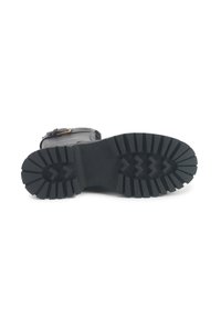 Stivale in pelle nera sdraiato su un lato che mostra una suola spessa e resistente con profonde scanalature e una fibbia laterale.