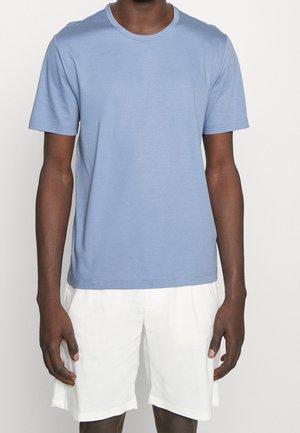 Jasnoniebieska bawełniana koszulka z okrągłym dekoltem i krótkimi rękawami, o gładkiej fakturze i minimalistycznym wzornictwie. W połączeniu z białymi szortami.