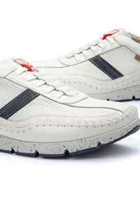 Sneakers bianche in pelle con pannelli forati, strisce laterali blu navy, cuciture beige e suola in gomma maculata. Accento rosso sui lacci.