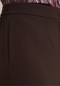 Close-up of dark brown elastic waistband pants worn with a purple and white patterned shirt tucked in.