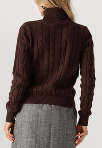 Bruine kabelgebreide coltrui met geribde manchetten en onderrand. Kenmerkt zich door een textuurpatroon en een aansluitend ontwerp. Draag het over een grijze geruite rok.