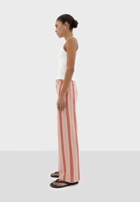 Gestreepte wijde broek in koraal en roze, gemaakt van lichtgewicht stof. Draag met een witte aansluitende tanktop en zwarte slippers. Zijaanzicht.
