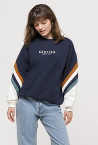 Marineblå sweatshirt med hvide, brune og teal stribede ærmer. Har rund halsudskæring og "KAOTIKO" logo på forsiden. Casual pasform.