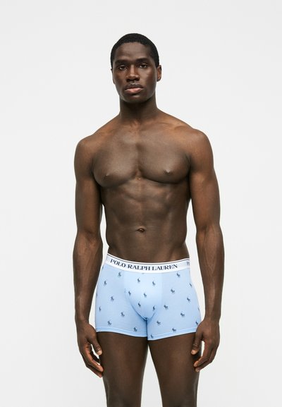 Μυώδης άνδρας που φοράει ανοιχτό μπλε boxer briefs Polo Ralph Lauren με μικρά σκοτεινά μοτίβα λογότυπου, στέκεται σε απλό φωτεινό φόντο.