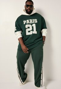 Green oversized jersey with "PARIS 21" in white, paired with matching pants featuring side snaps and white accents, made from a soft fabric.