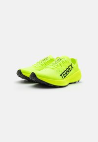 Limegrønne løbesko med sort "TERREX" branding, mesh-overdel, flade snørebånd og struktureret gummisål for greb.