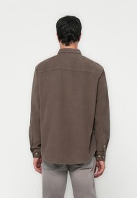 Chemise marron à manches longues avec un col, texture douce, poignets boutonnés et Ourlet droit, présentant un motif rayé subtil.