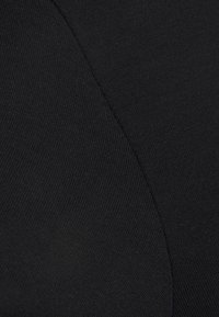Gros plan sur un tissu noir montrant une couture avec deux textures de tricot différentes se rejoignant sur une ligne inclinée.