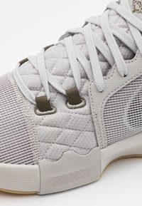 Baskets gris clair avec tissu matelassé, panneaux en mesh et accents texturés. Dotées de lacets plats et d'œillets renforcés. Semelle en caoutchouc.