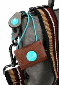 Grijze leren tas met een gestructureerde afwerking, voorzien van een veelkleurige gestreepte schouderband en een bruine leren label met een turquoise logo.