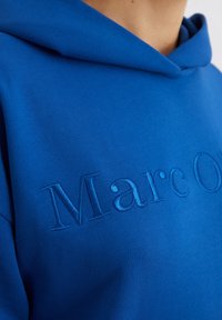 Felpa blu realizzata in tessuto morbido con testo ricamato in rilievo "Marc O'" in una tonalità di blu leggermente più chiara.