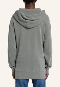 Huvtröja i dämpad grå, med en avslappnad passform, mjuk textur, långa ärmar och ribbade manschetter och nederkant. Bakvy visar huva.