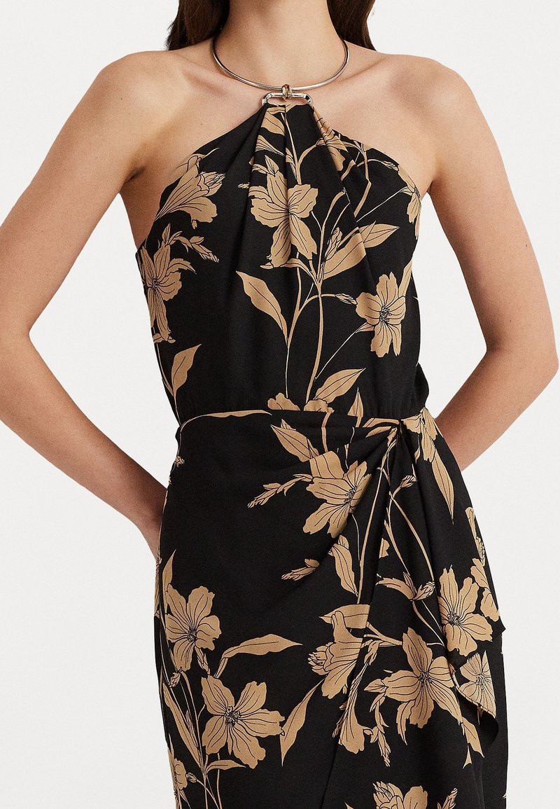 Femme portant une robe noire à col halter avec un motif floral beige et un détail d'anneau en argent au niveau de l'encolure.