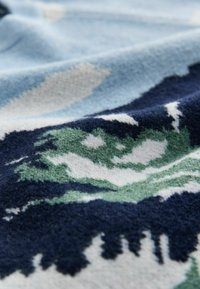 Tkaný plaid s jemným, textúrovaným dizajnom v modrej, zelenej a bielej farbe, zobrazujúci abstraktné vzory a vrstvené listy.
