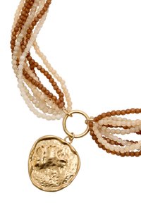 Naszyjnik z wieloma rzędami koralików w kolorach jasnobrązowym, kremowym i przezroczystym. Zakończony teksturowanym złotym wisiorkiem przymocowanym za pomocą okrągłego łącznika.