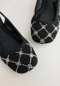 Sorte slip-on sko med et struktureret stof, der har et diamantmønster af sølvfarvede palietter og en glat sort indvendig.