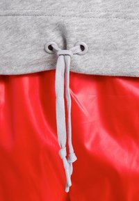 Grå sweatshirt-tyg med en röd glansig nederdel, med en grå dragsko som trädd genom metallöglor för justerbar passform.