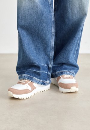 Sneaker bianche e rosa con un design testurizzato, chiusura con lacci e suole rigate; indossate con pantaloni in denim blu a vestibilità ampia.