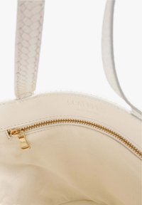 Interior de un bolso de cuero crema con un bolsillo de cremallera dorada y correas de cuero texturizado a juego.