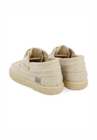 Zapatos slip-on de lona beige con parte superior texturizada y un interior suave. Suela de goma en color claro con detalle trenzado. Etiqueta de la marca visible en el costado.