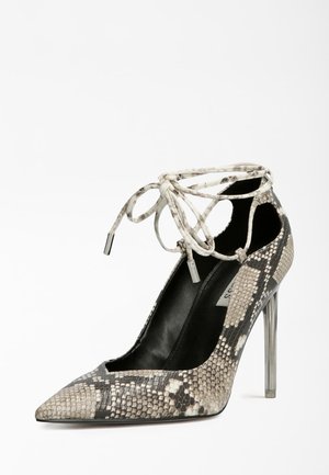 Chaussure à talon stiletto à bout pointu avec motif peau de serpent et brides à lacets à la cheville en tons beige, noir et gris sur fond blanc.