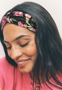 Blumen-Haarreifen mit schwarzer Basis und rosa sowie grünen Blumen, die zu glattem, dunklem Haar passen. Der Hintergrund ist neutral und weich.