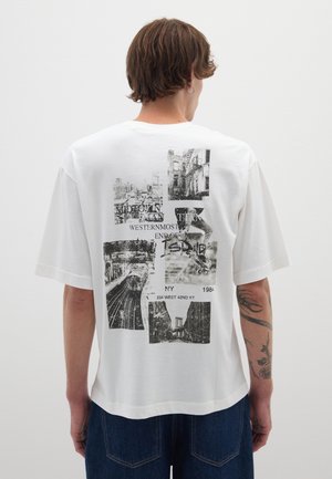 Camiseta de algodón blanca con diseño oversize, que presenta gráficos en negro de monumentos de Nueva York y texto en la parte trasera. Manga corta, corte relajado.