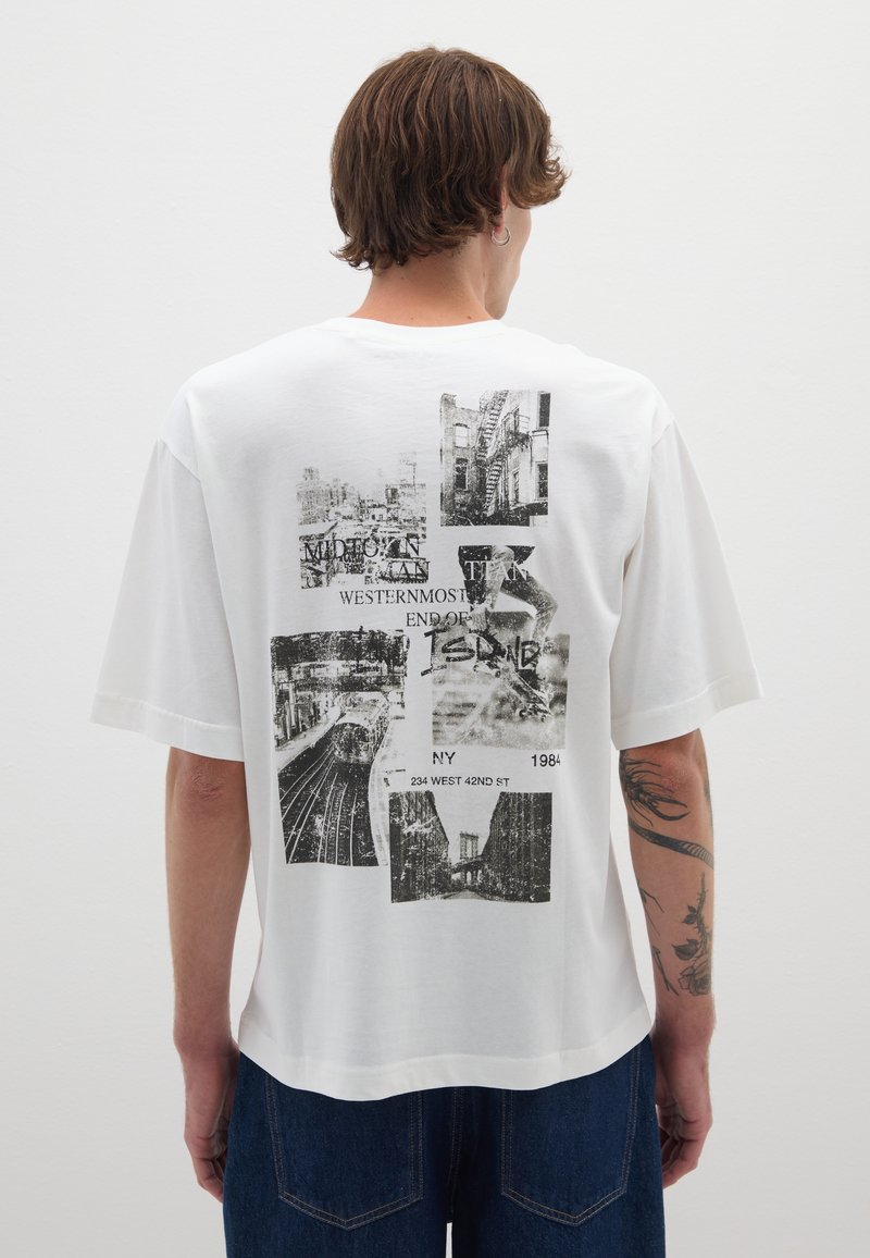 Camiseta de algodón blanca con diseño oversize, que presenta gráficos en negro de monumentos de Nueva York y texto en la parte trasera. Manga corta, corte relajado.