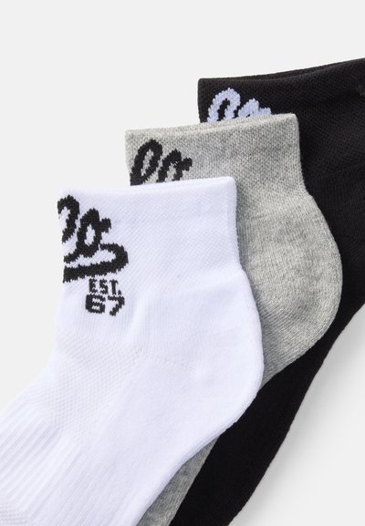 Tres pares de calcetines tobilleros en blanco, gris y negro, con un tejido de punto texturizado y un logo bordado con el año "87" en los puños.