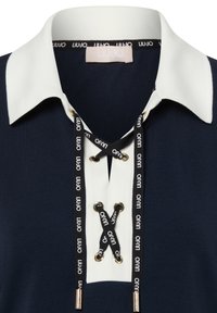 Marineblauw poloshirt met een witte kraag, een vetersluiting met een zwart lint met merktekst, en metalen accenten voor een veilige sluiting.