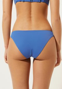 Blå bikiniunderdel med en slät textur, med en låg midja och minimal täckning bak. Inga framträdande mönster eller hårdvarudetaljer.