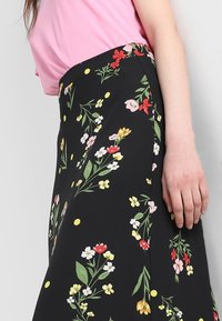 Černá květinová sukně s barevnými květy a žlutými puntíky, vyrobená z lehké látky s hladkým povrchem a detaily na bočních švech.