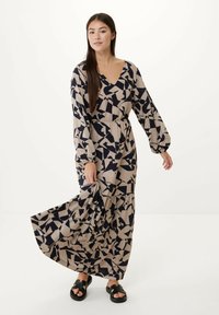 Maxi šaty v béžové barvě s námořnickými abstraktními geometrickými vzory, s dlouhými rukávy, véčkovým výstřihem a elastickým pasem pro volný siluetu.