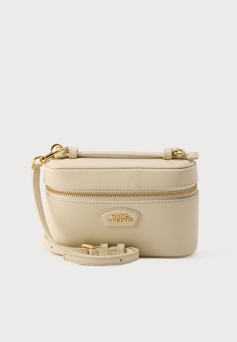 Sac bandoulière en cuir beige avec fermeture éclair, ferrures dorées et bandoulière ajustable. Présente un logo en relief sur le devant.