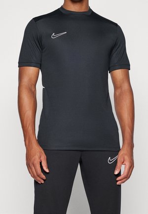 Mężczyzna noszący prostą czarną krótką sportową koszulkę i spodnie z białymi logo Nike swoosh na piersi i lewej udzie.