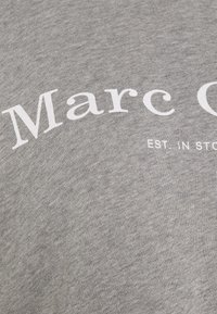 T-shirt grigia in cotone con un audace testo bianco che recita "Marc O'Polo" e "EST. A STOCCOLMA" sottostante in un carattere più piccolo.