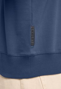 Marineblauer Sweatshirt mit geripptem Saum und Ärmelbündchen. Mit einem schwarzen Markenlabel an der Seite ausgestattet, hat es eine glatte Oberfläche und ein lässiges Design.