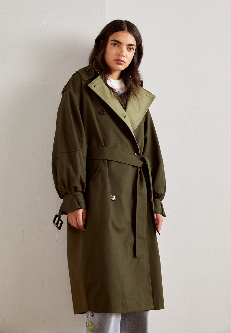Olivgrüner Trenchcoat mit doppelreihiger Knopfleiste, großen Revers, tailliertem Gürtel und elastischen Bündchen. Glattes Material mit klassischer Passform.