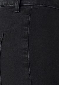 Calças de ganga pretas com um primeiro plano da textura do tecido, costura visível e detalhe do bolso lateral. Design suave e ajustado.