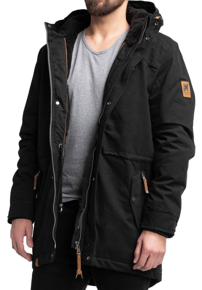 Sort parka med en struktureret, blød inderside, patch-detalje på ærmet, lynlås foran og trykknapper, med to forlommer.
