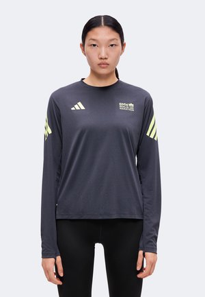 Jeune femme aux cheveux foncés en queue de cheval portant un t-shirt BMW Berlin Marathon à manches longues sombre avec des logos Adidas néon sur les manches et la poitrine.