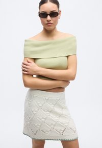 Õlgadest paljastav, soonikkoes heledalt rohelise tooniga top ning lühike valge kootud seelik, millel on teemantmuster ja roheline ääris. Mustad päikeseprillid peas.