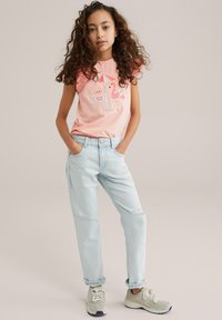 Camisa corta de manga corta en rosa claro con detalles de volantes y gráfico de flamenco; combinada con jeans ajustados en azul claro y zapatillas beige.