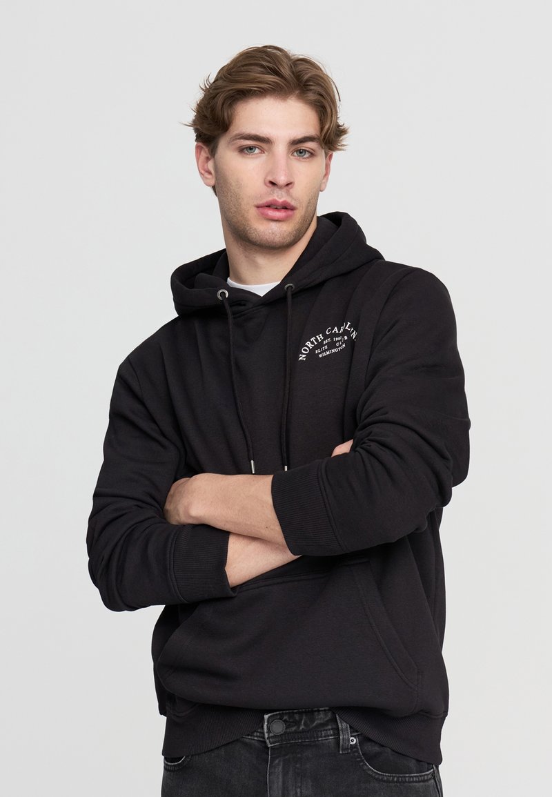 Czarna bluza z kapturem, z kangurzą kieszenią z przodu, sznurkiem w kapturze oraz białym logo po lewej stronie klatki piersiowej. Wykonana z miękkiego, teksturowanego materiału.