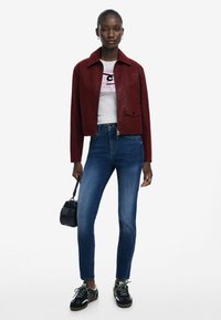 Veste cropped en cuir bourgogne avec un col, associée à un t-shirt graphique blanc, un jean slim bleu et des baskets noires. Petit sac noir.
