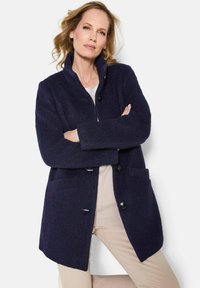 Cappotto elegante in misto lana di colore blu navy con colletto alto, chiusura a bottoni e due tasche frontali. Tessuto morbido e design dal taglio rilassato.