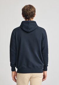 Sudadera azul marino hecha de tela suave, con capucha ajustable, puños y dobladillo acanalados, de corte relajado y sin logotipos visibles.