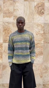 Knit sweater with horizontal stripes in gray, blue, and yellow, paired with black loose-fitting shorts. Texture appears soft and cozy.